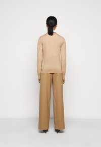 Beiger Strickpullover mit langen Ärmeln, rundem Ausschnitt und geripptem Saum, kombiniert mit weit geschnittenen, sandfarbenen Hosen aus glattem Stoff.