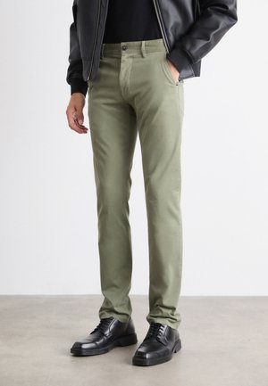 Olive green pants with a slim fit, made from soft cotton. Features five pockets and a metal button closure, paired with black shoes.