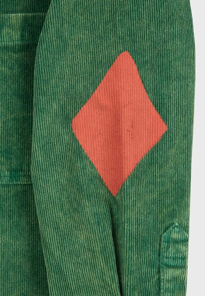 Grüner Cordstoff mit einem roten, diamantförmigen Patch, der auf die Oberfläche genäht ist.