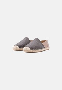 Paire d'espadrilles à enfiler avec l'avant texturé foncé, embout beige tissé, et détail du talon lisse brun clair sur fond uni.