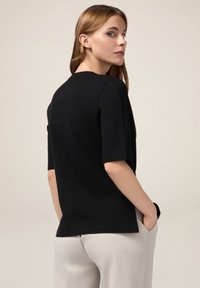 Top scurt negru, din bumbac, cu decolteu rotund, croială lejeră și detalii de cusătură la umeri.