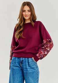 Bordowy sweatshirt z rękawami w kwiatowy wzór, o luźnym kroju i ściągaczach, w zestawie z niebieskimi dżinsami z wysokim stanem.