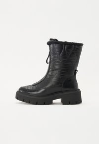 Bottines noires matelassées avec une finition texturée, un bord en fausse fourrure et une semelle épaisse et rayée. Présente un design à enfiler avec une languette.