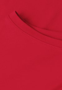 Gros plan d’un tissu en coton rouge avec un ourlet plié visible et un détail de couture sur un vêtement.