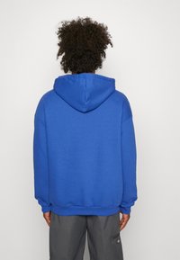 Felpa con cappuccio blu dalla texture morbida, taglio oversize e cappuccio con coulisse. Polsini e orlo presentano dettagli a coste.