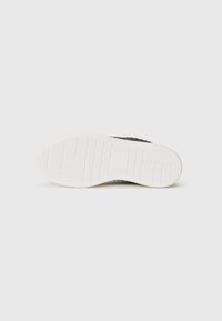 Sneaker nera con tomaia texturizzata e suola in gomma bianca, caratterizzata da un motivo a griglia per la trazione e un design moderno e filante.