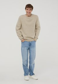 Beżowy sweter z dzianiny o okrągłym dekolcie, w połączeniu z jasnoniebieskimi dżinsami i białymi trampkami. Sweter ma ściągacze na rękawach i na dolnym brzegu.