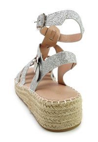 Glanzende zilveren sandaal met kruislings banden, enkelgesp en een gevlochten jute platform. Soepele beige binnenzool met stikdetails.