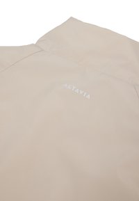 Chaqueta beige por detrás con cuello levantado y logo blanco "ALTAVIA" impreso debajo del cuello.