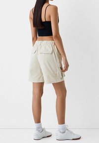 Beige cargo šortky s elastickým pasem, dvě postranní kapsy a dvě zadní kapsy, spárované s černým crop topem a bílými teniskami.