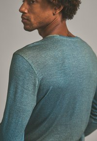 Turquoise long-sleeve shirt in a textured fabric, featuring a crew neckline and smooth shoulder seams, viewed from the back.