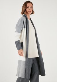 Cardigan lungo e aperto sul davanti in sfumature di grigio e bianco, con maniche a contrasto, morbido tessuto lavorato a maglia e fessure laterali per facilitare il movimento.