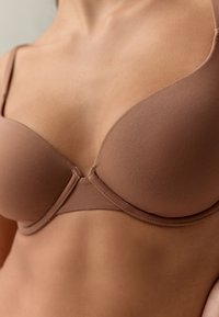 Helepruun polsterdatud rinnahoidja, sileda kangaga, raami toestusega ja reguleeritavate rihmadega, ilma nähtavate sulguriteta ja õmblusteta disainiga.