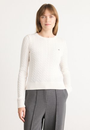 White cable-knit sweater with a round neckline and ribbed hem, featuring subtle brand logo on the left chest. Smooth texture.