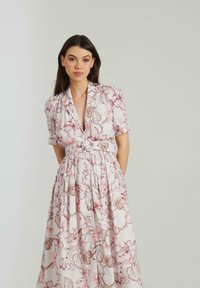 Abito midi floreale in rosa chiaro e bianco, con maniche corte, scollatura a V profonda, vita cinturata con un bottone decorativo e gonna plissettata.