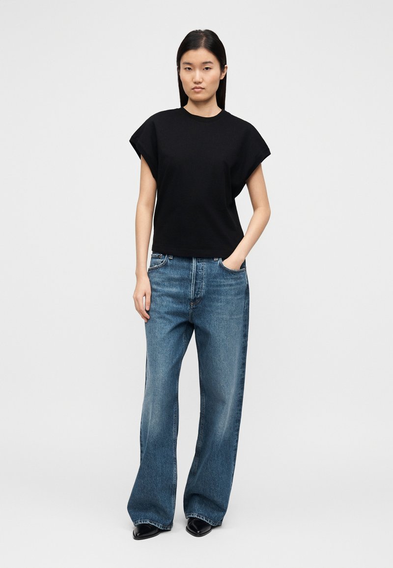 Haut noir à manches courtes avec une coupe décontractée, associé à un jean bleu clair à jambes larges, mettant en valeur un design casual et la texture du denim.