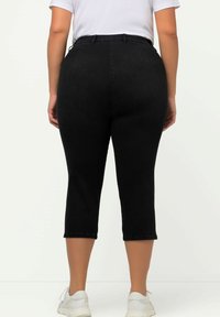 Pantalones capri de mezclilla negros con una cintura alta, textura ligeramente elástica y un corte cropped, combinados con zapatos deportivos blancos.