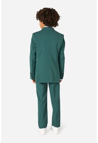 Completo verde per bambini con giacca su misura e pantaloni coordinati, realizzato in tessuto morbido. Presenta polsini di camicia bianchi e semplici dettagli con bottoni.