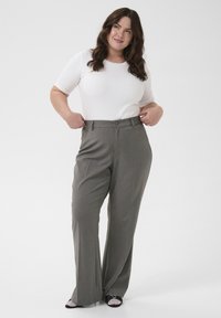 Pantalons gris à jambes larges avec une texture lisse et un devant plissé, associés à un haut blanc ajusté en côtes. Fermeture simple à deux boutons.
