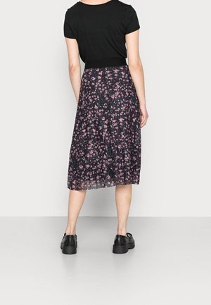 Sort top med korte ærmer kombineret med en midilængde nederdel med et mørkt blomsterprint i rosa og blå nuancer på et gennemsigtigt stof. Sorte sko.