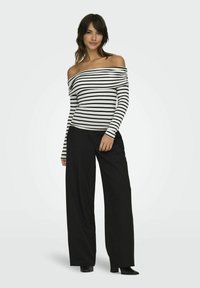 Off-shoulder stribet top i sort og hvid, med lange ærmer, parret med løstsiddende sorte bukser og sorte hælstøvler.