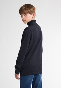 Dunkelblauer Rollkragenpullover, gestricktes Material, lange Ärmel, gerippte Bündchen und Saum, einfarbig, schlichtes Design. Kombiniert mit blauen Jeans.