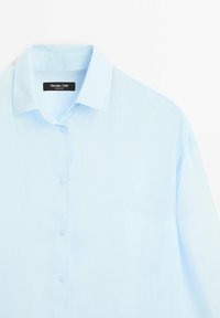 Camicia a maniche lunghe azzurro chiaro realizzata in tessuto morbido. Presenta un colletto a punte e una chiusura con bottoni frontale con sei bottoni e un design dalla vestibilità rilassata.