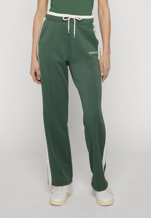 Grønne bukser med vide ben, hvide sidelommer og snørre i taljen, båret med hvide sneakers og grøn top, stående på neutral baggrund.