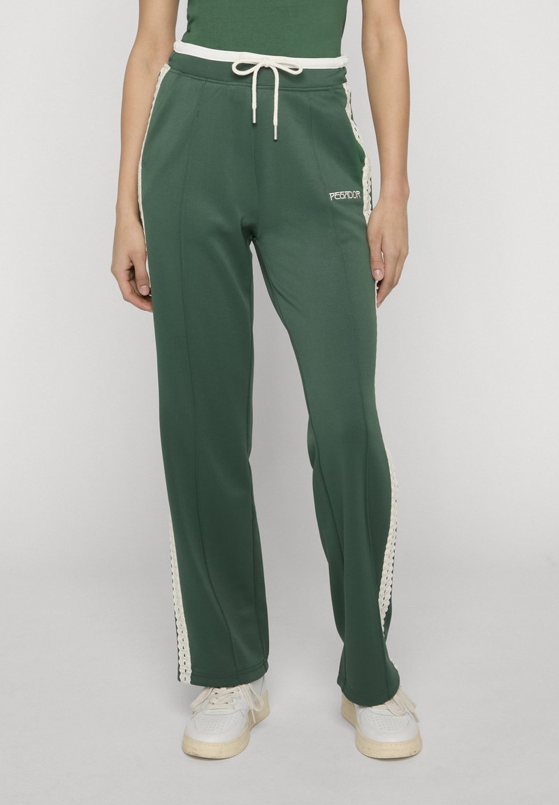 Zielone spodnie o szerokich nogawkach z białymi paskami po bokach i ściągaczem w talii, noszone z białymi trampkami i zielonym topem, stojące na neutralnym tle.