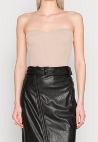 Beige ribbad strapless bodysuit med hjärtformad axelutskärning, kombinerad med en svart läderkjol med hög midja som har en sidoren och bälte.