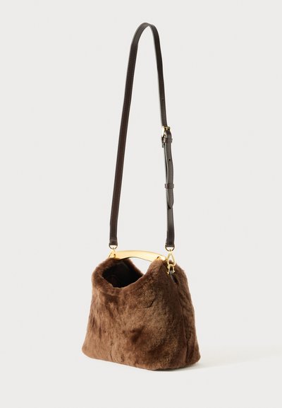 Pruunist karvast käsitasku, millel on kõver kullast riistvara käepide ja eemaldatav pruun nahast rihm. Tekstuuriga, pehme karvane viimistlus.