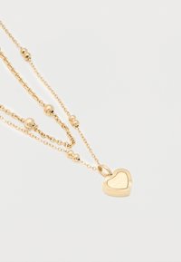 Χρυσά στρωματοποιημένα κολιέ με μικρές χρυσές χάντρες και μενταγιόν σε σχήμα καρδιάς, σκαλισμένο με τη φράση "Tommy Hilfiger 1985".