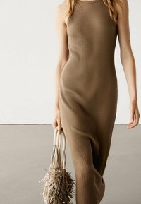 Robe sans manches côtelée de couleur marron chaud, avec une silhouette ajustée. Accessoirisée d'un sac à main texturé de tonalité neutre.