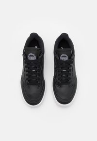 Ett par svarta lädersneakers med svarta snören och vita sulor, sedd ovanifrån på en vit bakgrund.