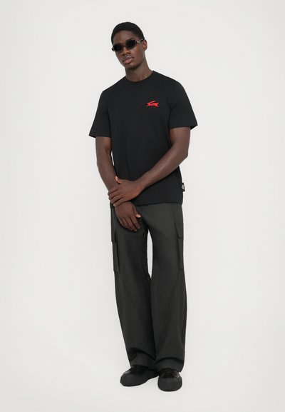 Sort bomulds t-shirt med rødt logo, parret med løse grå cargo bukser med sidelommer og en afslappet silhuet.