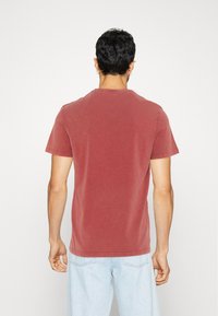T-shirt a maniche corte, con collo a giro, di cotone rosso sbiadito, caratterizzato da una vestibilità comoda e dettagli di cucitura sottili. Vista posteriore mostrata.