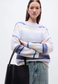 Pull rayé en bleu clair, crème et marine, fabriqué en matière douce. Associé à un sac seau en cuir noir et un jean bleu clair.
