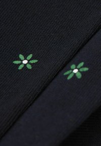 Granatowy dzianinowy materiał prezentuje dwa zielone wzory haftów kwiatowych z białymi środkami. Tekstura jest gładka, z delikatnymi szczegółami w prążki.