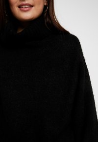 Černý nadměrný svetr s žebrovaným rolákem, vyrobený z měkké texturované látky a s designem s klesajícími rameny. Minimalistický styl.