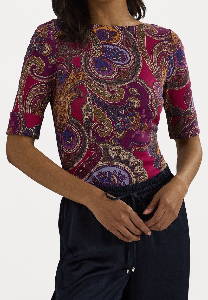 Mujer vistiendo una blusa ajustada de media manga con un patrón de paisley multicolor, combinada con pantalones holgados negros con cordón.