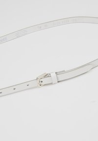 Cintura in pelle bianca con fibbia in metallo argentato, presenta cinque fori per la regolazione e il nome del marchio impresso sul lato interno.