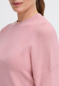 Pink knit sweater featuring a ribbed texture, round neckline, and relaxed fit. The fabric appears soft and lightweight with a subtle sheen.
