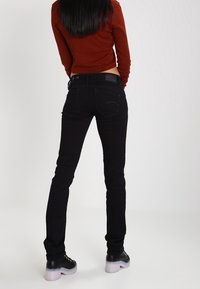 Jean slim noir avec un design classique à cinq poches, présentant une texture lisse et des détails de couture subtils, portés avec des bottes noires.