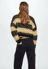 Maglione lavorato a maglia con audaci strisce nere, gialle e bianche, caratterizzato da un design corto e un tessuto testurizzato. Indossato con pantaloni cargo neri.