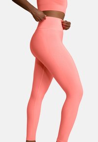 Legginsy o wysokim stanie w jasnym koralowym kolorze, teksturowana tkanina z pionowymi prążkami po bokach, przylegający krój, bezszwowy pas.