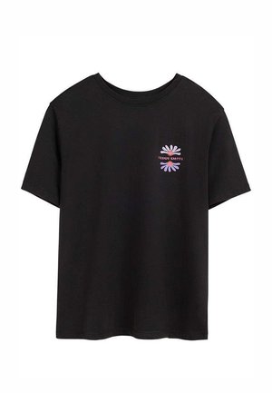T-shirt noir à manches courtes avec un petit motif de fleur violette et le texte "TEDDY SMITH" sur le côté gauche de la poitrine.