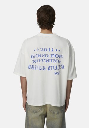 Maglietta bianca oversize con stampa blu testurizzata sul retro, con la scritta "2011 GOOD FOR NOTHING BRITISH ATELIER" e stelle.