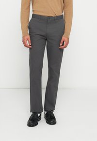 Γκρι παντελόνι σε στενή γραμμή από ελαφρύ ύφασμα, με ίσια μπροστινή όψη και κανονική μέση. Συνδυάζεται με μαύρα μοκασίνια.