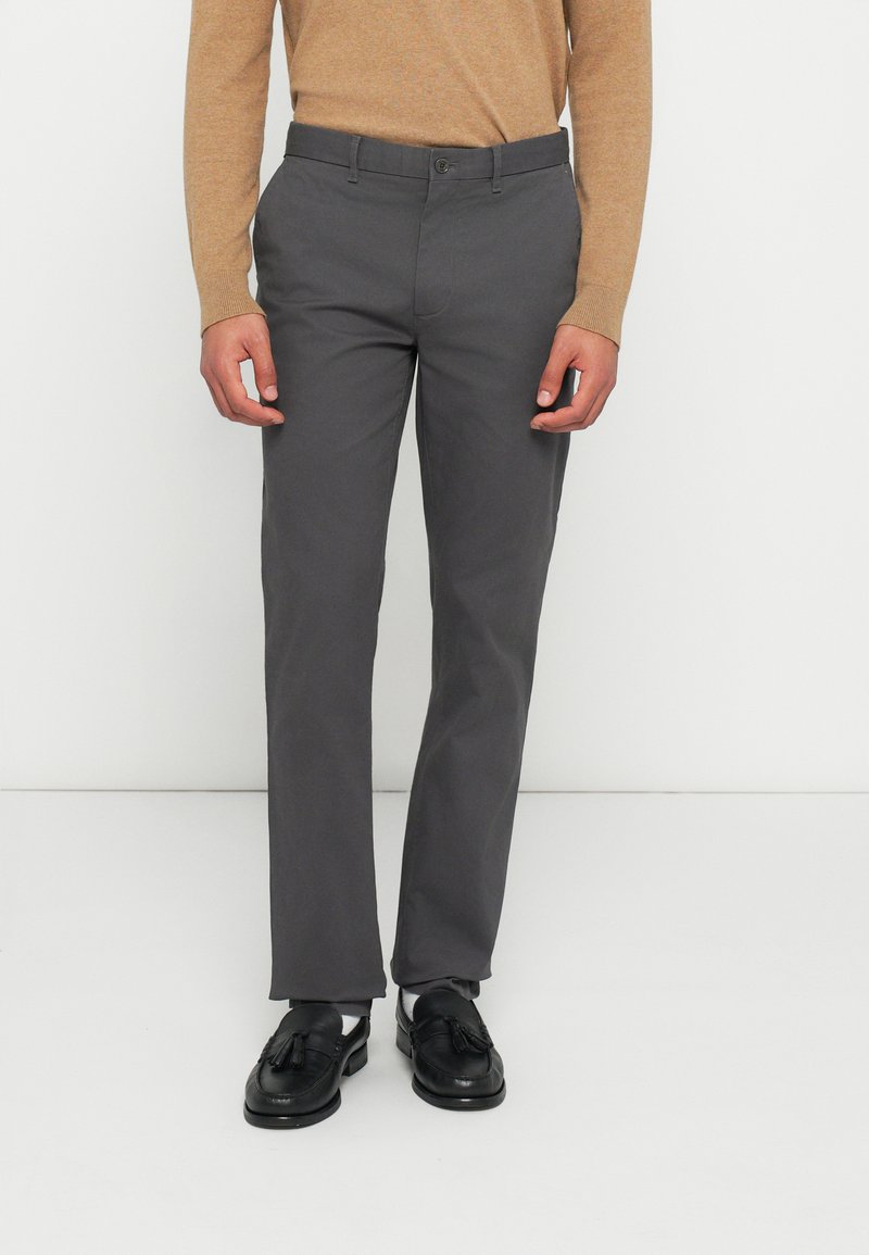 Γκρι παντελόνι σε στενή γραμμή από ελαφρύ ύφασμα, με ίσια μπροστινή όψη και κανονική μέση. Συνδυάζεται με μαύρα μοκασίνια.