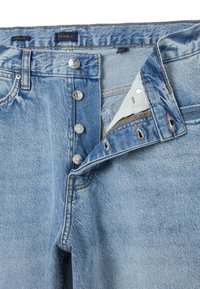Jeans de mezclilla de corte ancho en azul claro con cierre de cinco botones, costuras visibles y bordes deshilachados. Textura suave con un acabado ligeramente desgastado.